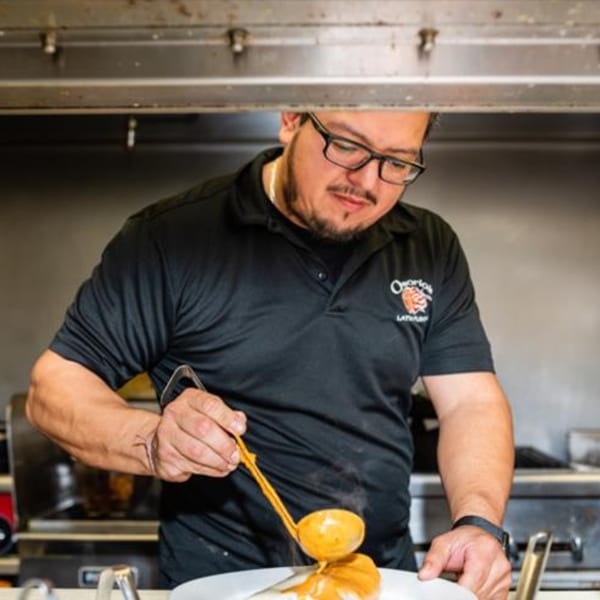 Osorio's Latin Fusion chef in glasses and black polo, ladling sauce onto a dish.