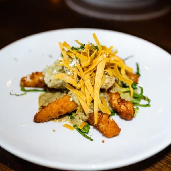 Crispy fried Mexican chicken tenders with green sauce, cheese, and tortilla strips on a white plate.