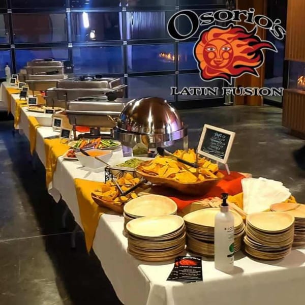 A buffet table with Osorio's Latin Fusion logo, serving Mexican food like chips, dips, and hot dishes.