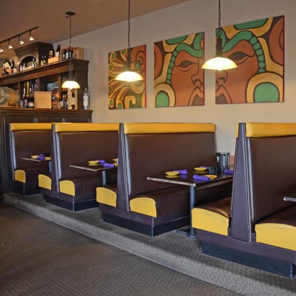 Osorio's Latin Fusion dining room with brown and yellow booths, colorful wall art, and a bar.