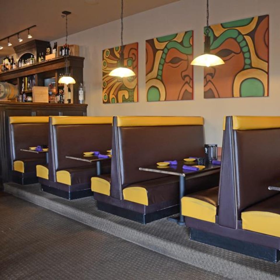 Osorio's Latin Fusion dining room with brown and yellow booths, colorful wall art, and a bar.
