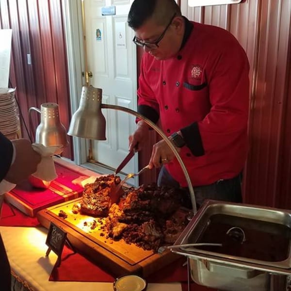 A chef in a red jacket carves prime rib under heat lamps at Osorio's Latin Fusion.