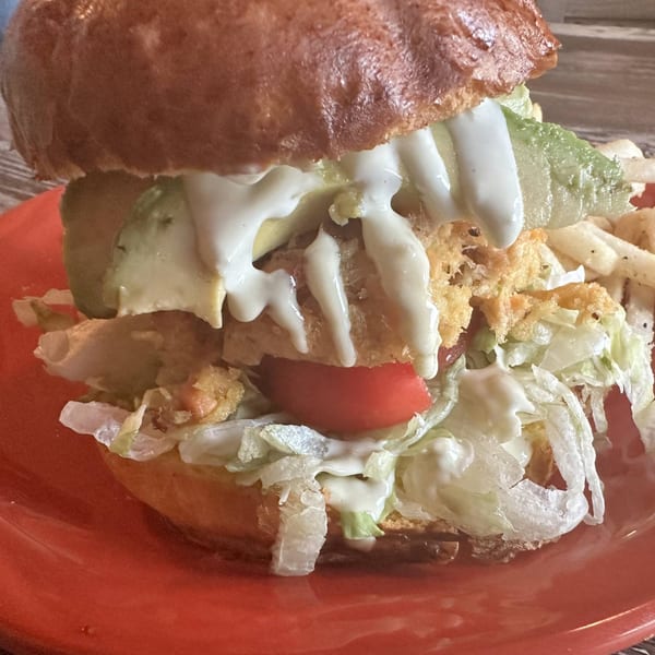 A close-up of a large Osorio's Latin Fusion burger with avocado, lettuce, tomato, and white sauce.