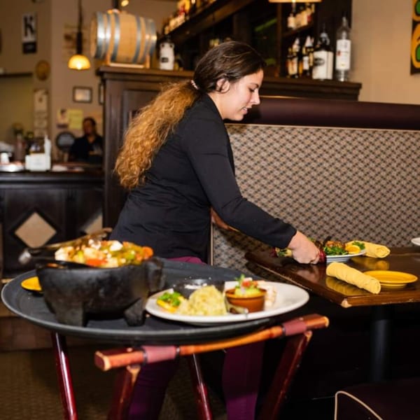 A server at Osorio's Latin Fusion places a plate of Mexican food on a table.