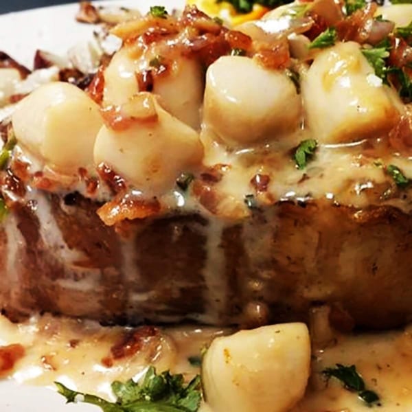 Close-up of seared scallops with a creamy sauce, bacon bits, and fresh herbs.