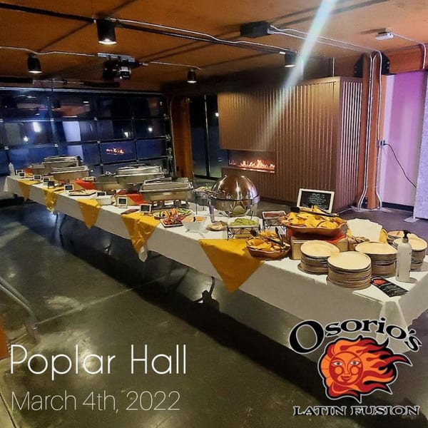 Osorio's Latin Fusion buffet table with Mexican food, chafing dishes, and a modern fireplace in the background.