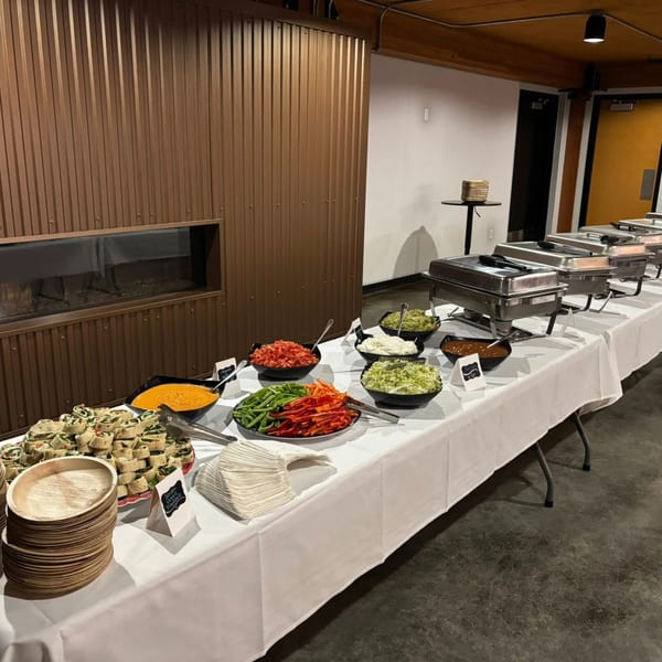 A buffet table with various Mexican dishes, including wraps, dips, chopped vegetables, and chafing dishes.