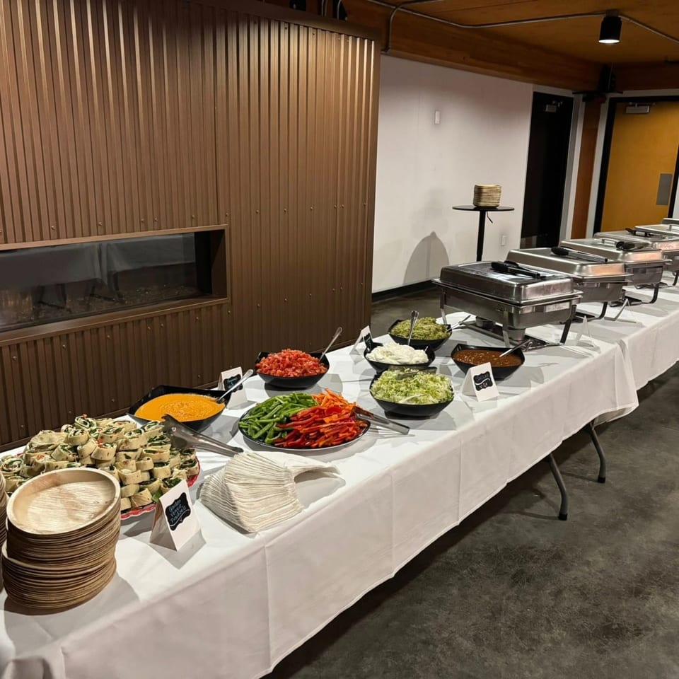 A buffet table with various Mexican dishes, including wraps, dips, chopped vegetables, and chafing dishes.