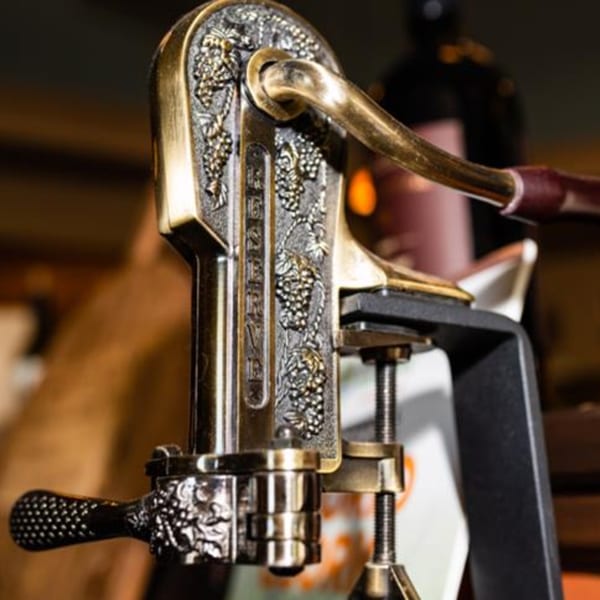 Close-up of an ornate, antique-style wine opener with grape vine detailing, ready for use.