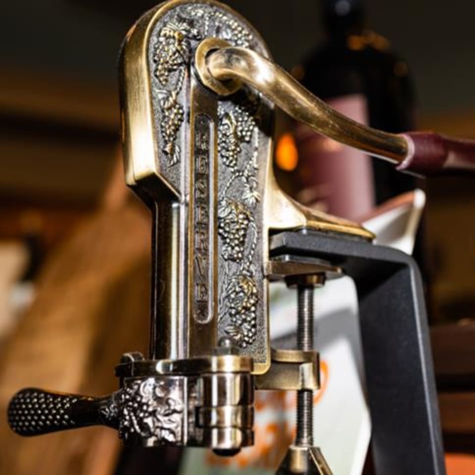 Close-up of an ornate, antique-style wine opener with grape vine detailing, ready for use.