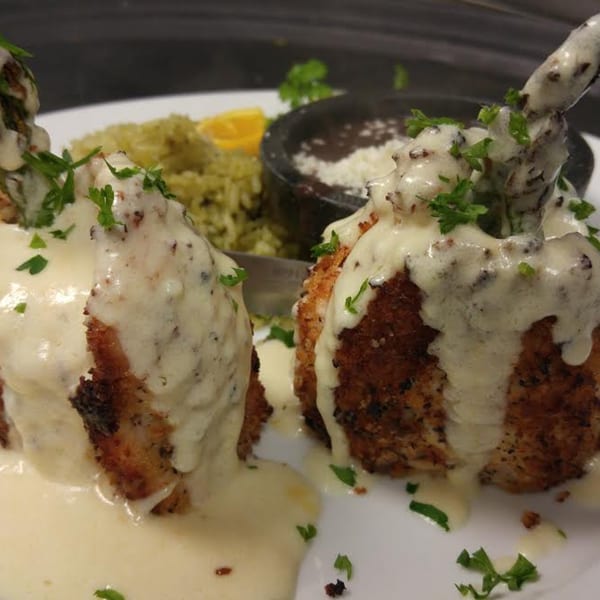 Two breaded chicken drumsticks covered in creamy white sauce and parsley, with rice and beans.