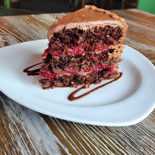 A slice of chocolate cake with raspberry filling and chocolate frosting on a white plate.