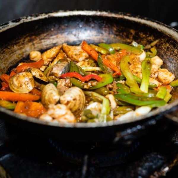 Sizzling Osorio's Latin Fusion fajitas with chicken, clams, bell peppers, and onions in a hot pan.