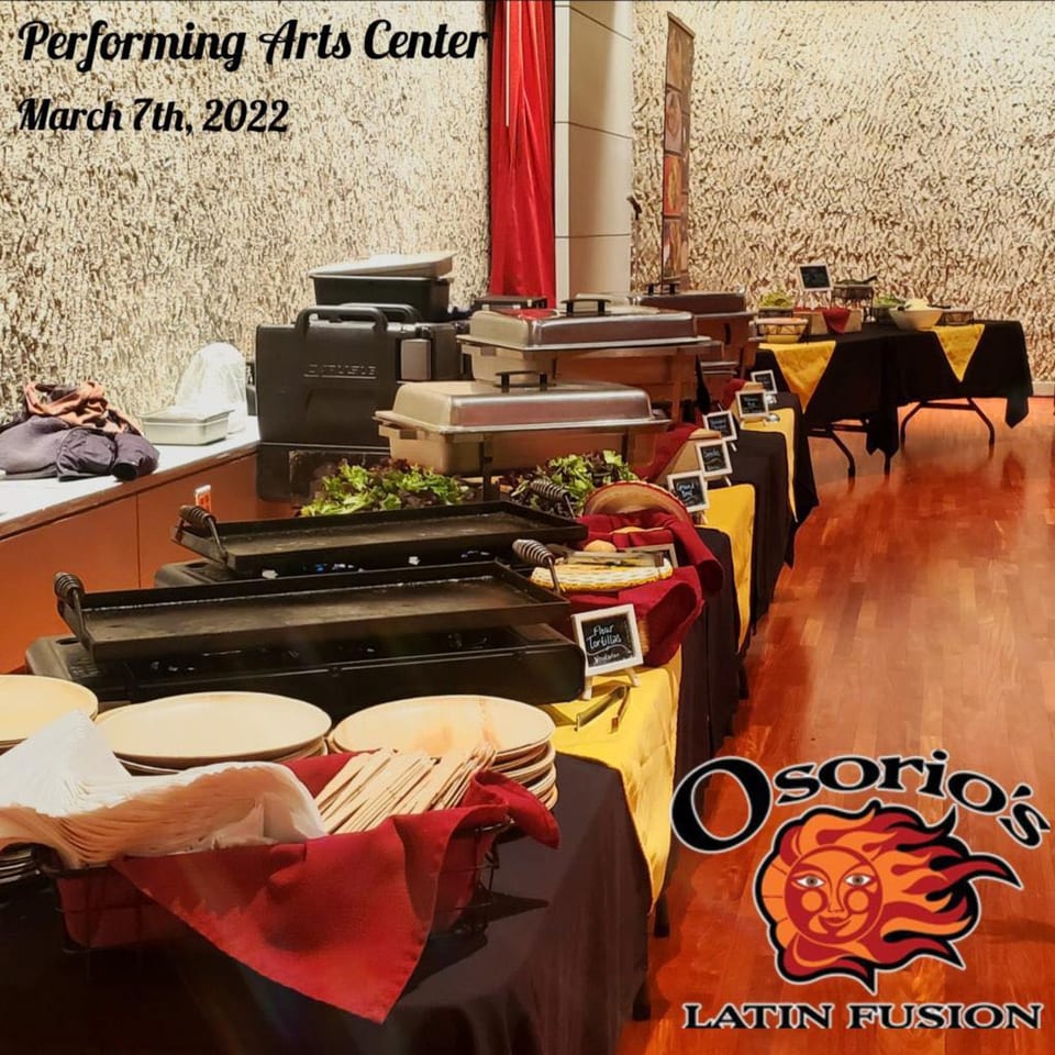 Osorio's Latin Fusion catering setup with chafing dishes, griddles, and serving ware on black and yellow tables.