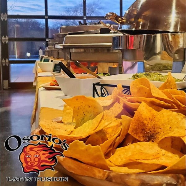 A buffet table with tortilla chips, guacamole, and other Mexican dishes in chafing dishes.
