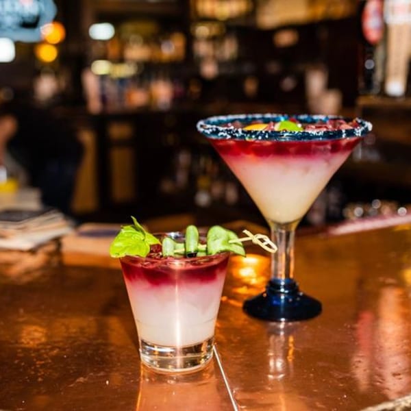 Two colorful Osorio's Latin Fusion cocktails, one a margarita, on a bar with a blurred background.