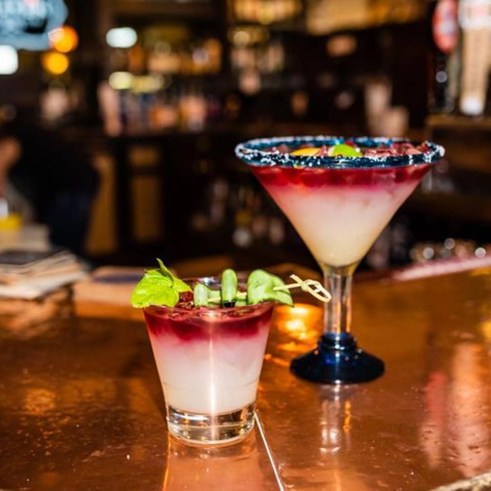 Two colorful Osorio's Latin Fusion cocktails, one a margarita, on a bar with a blurred background.