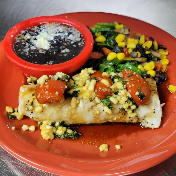 Osorio's Latin Fusion's fish entree with black beans, corn, and spinach on a red plate.
