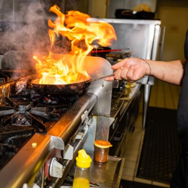 A chef's hand holds a pan with large flames rising from it on a stove.