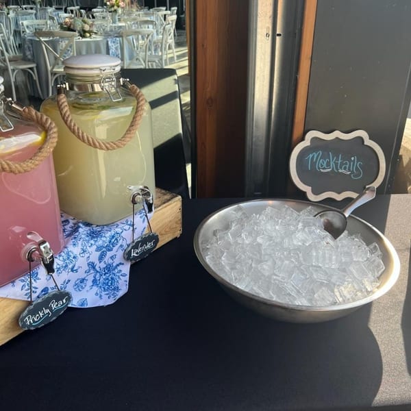Mocktail station with prickly pear and lavender drinks in dispensers, ice bucket, and a "Mocktails" sign.