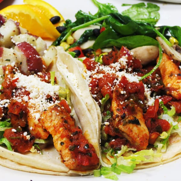 Two chicken tacos with salsa, cheese, lettuce, a side of potato salad, and spinach salad.