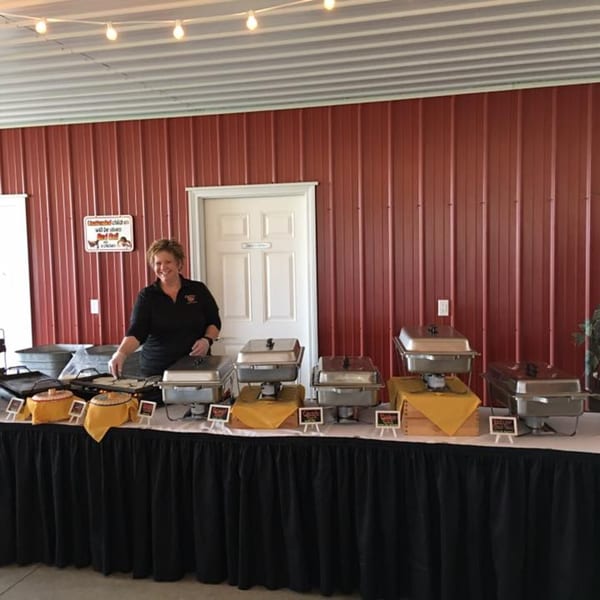 A smiling woman stands behind a buffet table with Osorio's Latin Fusion catering dishes.