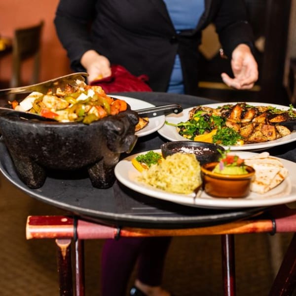 A server carries a tray with Osorio's Latin Fusion fajitas in a molcajete and other Mexican dishes.